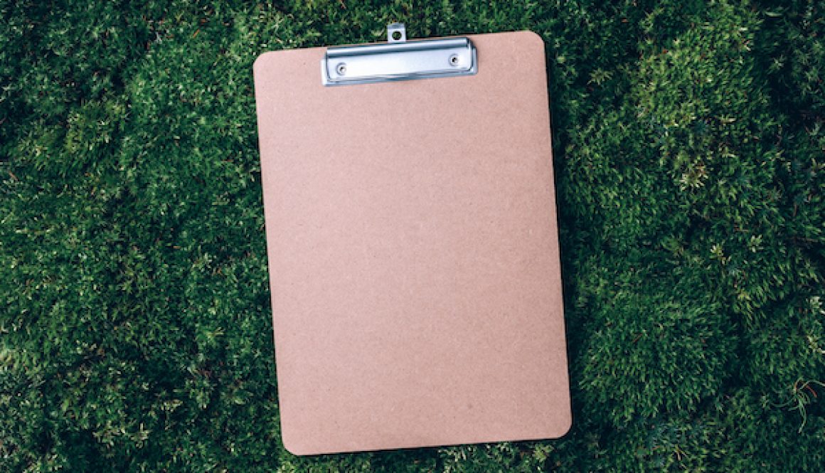 Top view of clipboard, paper, pen on green grass, moss background. Copy space. Flat lay. Office mock up, remote job. Wild nature, ecology concept. Sustainable, organic, zero waste lifestyle
