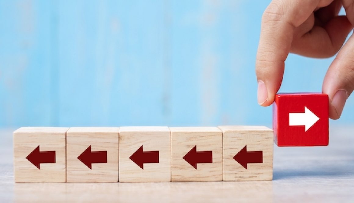 Businessman hand placing or pulling Red block with different direction of arrow on table background. Business Growth, Improvement, strategy, Successful, different and Unique Concepts