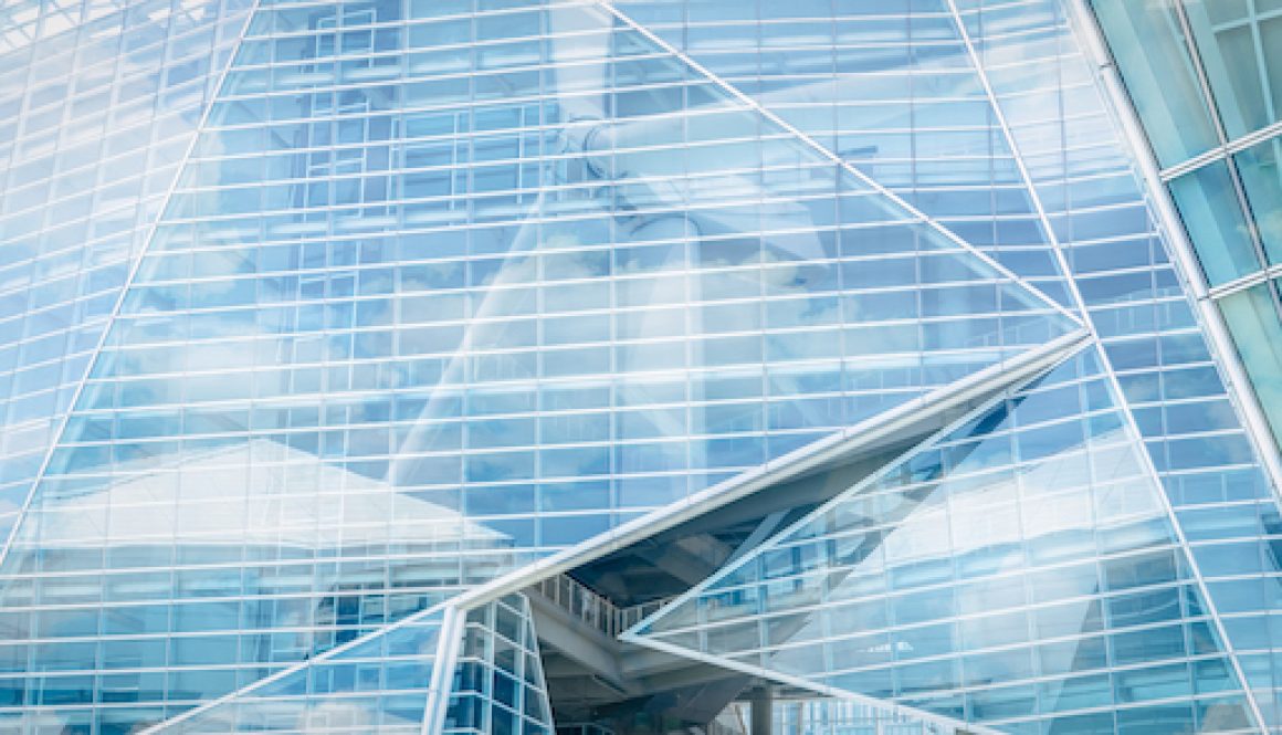 Sustainable glass building and wind power concept. Wind turbine and blue sky reflect on sustainable corporate office building. Green energy. Sustainable development goals concept. Renewable energy.