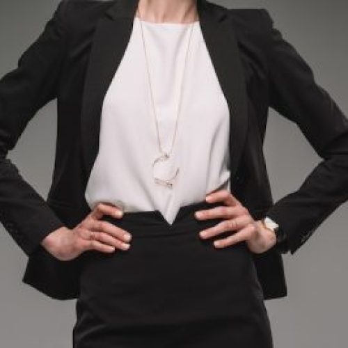 cropped image of businesswoman standing with hands on hips isolated on grey background