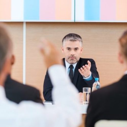 Everyone is welcome for discussion. Confident mature man in formalwear giving a word to someone from audience while sitting in conference hall